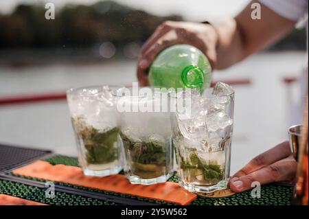 Erfrischende Mojito-Cocktails, die an einem sonnigen Tag am Wasser gegossen werden. Stockfoto