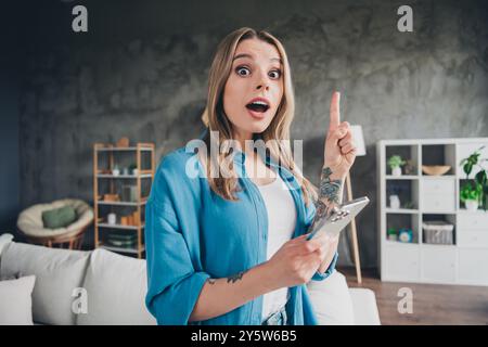 Foto einer jungen Geschäftsfrau, die ein blaues Hemd mit einem Smartphone in ihrem Loft-Büro trägt und mit dem Finger zeigt, der eine großartige Idee für Kunden hat Stockfoto