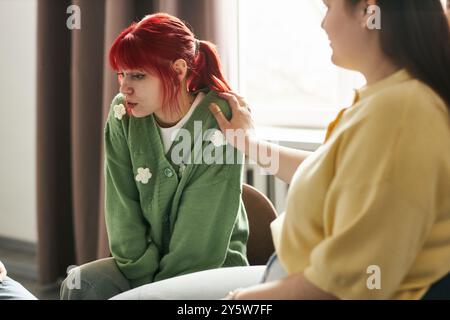 Eine Gruppe von Frauen sitzt auf Stühlen in einem gemütlichen Raum und führt lebhafte Gespräche mit warmem Ausdruck, Tageslicht strömt durch ein Fenster in der Nähe Stockfoto