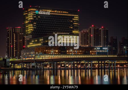 Cleveland Clinic Abu Dhabi. Das moderne Gebäude leuchtet mit Lichtern, die sich im Meer spiegeln. Die umliegenden Hochhäuser fügen sich in die Ruhe ein Stockfoto