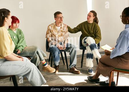 Verschiedene Gruppen von Einzelpersonen, die an einer Gruppentherapie teilnehmen, zuhören und in einer ungezwungenen Umgebung mit hellem Boden und entspannter Atmosphäre teilnehmen Stockfoto