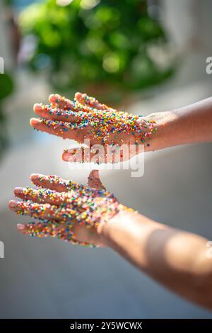 Klebrige weibliche Hände in bunten Streuseln für Cupcakes, Donuts, Kuchen im Sonnenlicht. Nachtisch Stockfoto