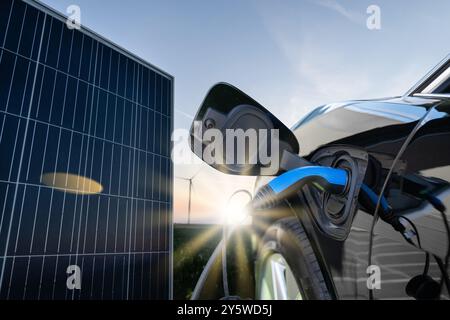 Nahaufnahme eines Elektroautos mit angeschlossenem Ladekabel auf dem Hintergrund von Solarpaneelen. Stockfoto