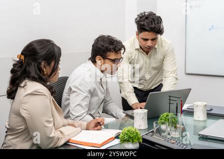 Dieses Foto zeigt eine vielfältige Gruppe von Fachleuten, die sich in einem Büroraum für ein produktives Meeting versammelt haben. Der Fokus liegt auf einem indischen Manager, der Stockfoto