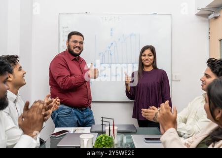 Ein Mitarbeiter feiert Erfolg und Motivation in einem Firmenbüro. Das vielseitige Büroteam applaudiert begeistert und feiert den gelungenen Acquis Stockfoto