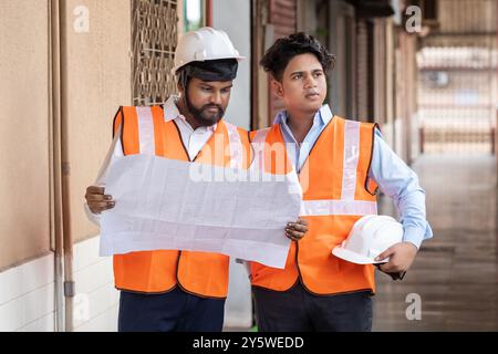 Zwei Ingenieure arbeiten auf einer Baustelle zusammen und diskutieren ausführlich über den Grundriss und die Baupläne des Projekts. Beide sind Stockfoto