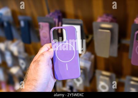 Paris, Frankreich - 20. September 2024: POV einer männlichen Hand, die Apples neue Beats Kunststoffhülle für iPhone 16 in lila Farbe mit Ladelinien hält, andere Hüllen im Hintergrund sichtbar Stockfoto