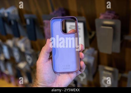 Paris, Frankreich - 20. September 2024: POV einer männlichen Hand, die Apples neue Beats Kunststoffhülle für iPhone 16 in lila hält, mit mehreren anderen Hüllen im Hintergrund Stockfoto