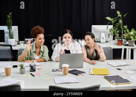 Drei Berufsfrauen führen ein lebhaftes Gespräch, während sie an ihren Schreibtischen arbeiten. Stockfoto