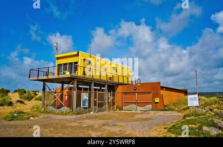 Eine leuchtend gelbe, erhöhte Rettungsschwimmer-Station befindet sich an einem Strand, der von Sanddünen und Gras umgeben ist Stockfoto