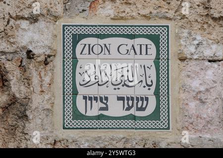 Ein Straßenschild mit Keramikfliesen auf einer alten Steinmauer in Hebräisch, Arabisch und Englisch in der Altstadt von Jerusalem, das den Eingang zum Zion-Tor markiert. Stockfoto