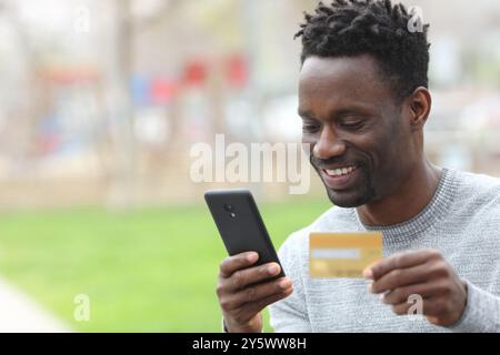 Glücklicher schwarzer Mann, der online mit Handy und Kreditkarte auf der Straße kauft Stockfoto