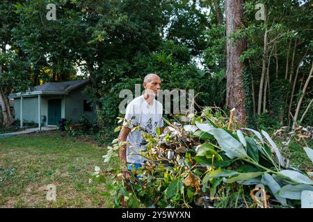 Ein erwachsener Mann steht inmitten von grüner Gartenschutte in einem Hinterhof, mit Blick zur Seite, mit einem Haus und Bäumen im Hintergrund, Florida, USA Stockfoto