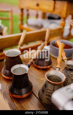 Traditionelle Kupferkaffeekannen mit Holzgriffen auf einem Holztisch im Freien. Stockfoto