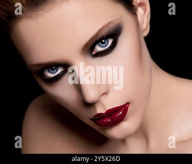 Porträt einer Frau in Nahaufnahme mit dramatischem rotem Lippenstift und rauchiger Augen-Make-up vor schwarzem Hintergrund. Stockfoto