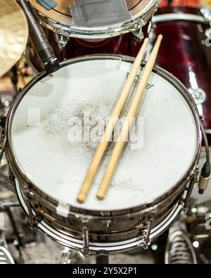 Nahaufnahme einer Snare-Trommel mit einem Paar hölzernen Drumsticks oben, umgeben von anderen Schlaginstrumenten. Stockfoto