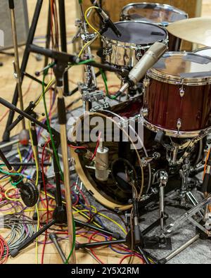 Nahaufnahme eines Drum-Sets, umgeben von Mikrofonen und bunten Kabeln auf einem hölzernen Bühnenboden. Stockfoto