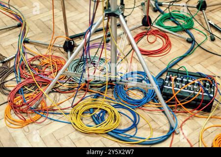 Bunte Kabel, die sich auf einem Holzboden verheddert haben, inmitten von Notenständern und Mikrofonständern. Stockfoto