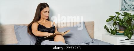 Eine zierliche brünette Frau entspannt sich in ihrem gemütlichen Schlafzimmer, tief vertieft in ein fesselndes Buch, während sie auf ihrem Bett sitzt. Stockfoto