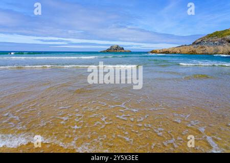 Kleine Wellen brechen an einem hellen Sommermorgen am Crantock Beach auf und blicken auf Goose Island. Stockfoto