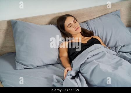 Eine junge brünette Frau, die ein kleiner Mensch ist, genießt zu Hause einen ruhigen Moment in weiche Decken gewickelt. Stockfoto