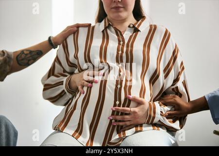 Die werdende Mutter sitzt bequem, während sie die Menschen umgibt, die sie unterstützen, indem sie sanft die Hände auf ihre Babypuppe legt, um die Pflege und die Vorfreude auf die Neuankömmlinge zu vermitteln Stockfoto