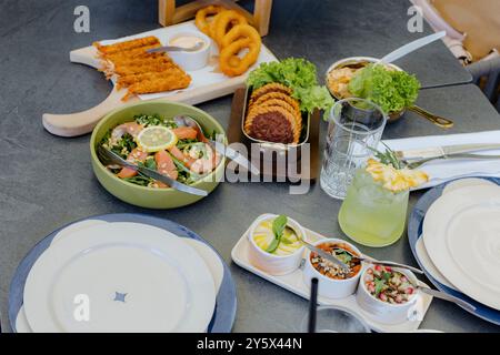 Ein Tisch mit verschiedenen Gerichten, darunter Salat, frittierte Vorspeisen und ein erfrischendes Getränk mit Ananasgarnitur. Stockfoto