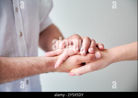 Nahaufnahme von zwei Händen, die eine zarte Berührung ausüben. Hände von Mann und Frau auf weißem neutralen Hintergrund. Der Mann hält die Hand seiner liebenswerten Frau. Konzept von Liebe, Intimität, Unterstützung und Vertrauen. Stockfoto