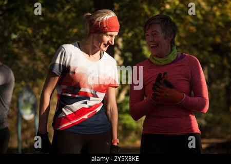 Zwei Frauen lächeln und sprechen während einer Outdoor-Übung in einem Park mit warmem Sonnenlicht. Stockfoto
