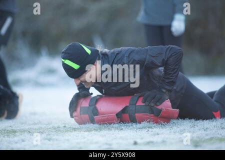 Person, die im Freien auf frostigem Gras eine HLW an einer Übungspuppe durchführt, mit einer anderen Person im Hintergrund. Stockfoto