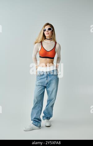 Eine selbstbewusste junge Frau trägt trendige Sommerkleidung und Sonnenbrille in einem minimalistischen Raum. Stockfoto