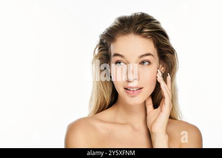 Die junge Frau berührt ihr Gesicht sanft und zeigt ihre natürliche Schönheit und ihre weichen Gesichtszüge. Stockfoto