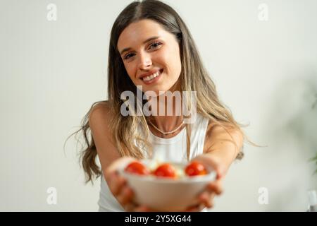 Porträt einer fröhlichen jungen Frau mit Ombre-Haar, die eine Schüssel frischen Salat anbietet. Bild vermittelt gesunde Essgewohnheiten, Hausmannskost und positive Atts Stockfoto