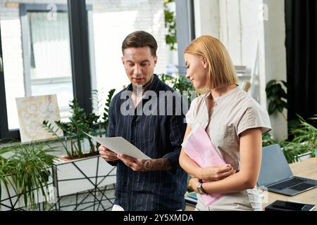 Zwei junge Kollegen diskutieren Projektdetails, während sie in einem lebhaften Büro von Grün umgeben sind. Stockfoto