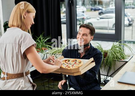 Zwei junge Kollegen teilen einen freudigen Moment, während sie während der Mittagspause Pizza genießen. Stockfoto