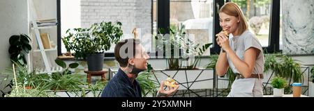 Zwei Kollegen teilen sich ein zwangloses Mittagessen, umgeben von Grün, Lächeln und plaudern. Stockfoto