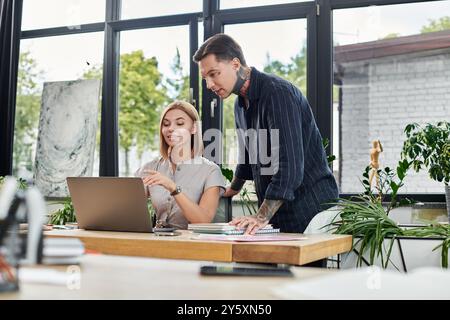 Zwei Kollegen führen ein lebhaftes Gespräch, während sie an ihrem Schreibtisch an einem Laptop arbeiten. Stockfoto