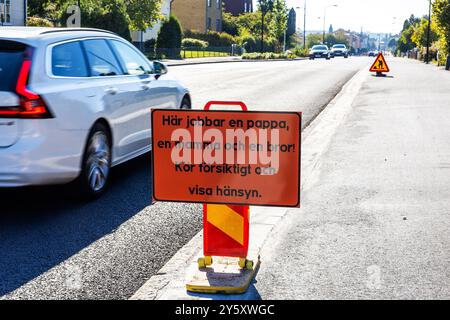 Informationen für Autofahrer, die während Bauarbeiten fahren. Hier ist ein Schild mit dem Text: Ein Vater, eine Mutter und ein Bruder arbeiten hier! Fahren Sie vorsichtig und seien Sie vorsichtig. (Auf schwedisch: Här jobbar en pappa, en mamma och en bror! KÖR försiktigt och Visa hänsyn). Stockfoto