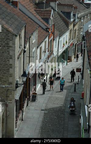 Blick von oben mit Blick auf die steilen Ziegeldächer der Häuser und Geschäfte auf dem Kopfsteinpflaster Catherine Hill in Frome Somerset an einem sonnigen Sommertag Stockfoto