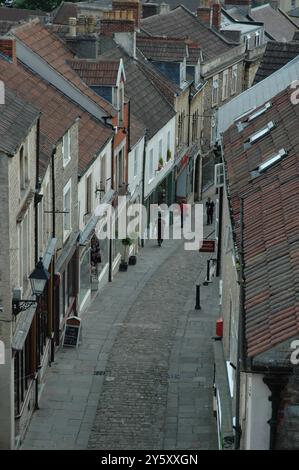 Blick von oben mit Blick auf die steilen Ziegeldächer der Häuser und Geschäfte auf dem Kopfsteinpflaster Catherine Hill in Frome Somerset an einem ruhigen Sommertag Stockfoto