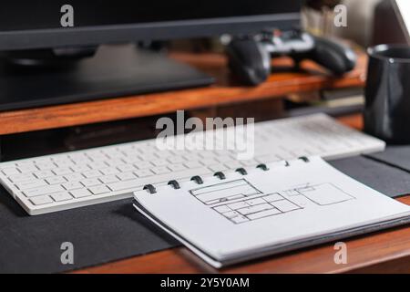 Ein moderner Arbeitsbereich mit Computermonitor, Tastatur, Skizzenblock und Gaming-Controller, der eine Mischung aus Kreativität und Technologie veranschaulicht Stockfoto