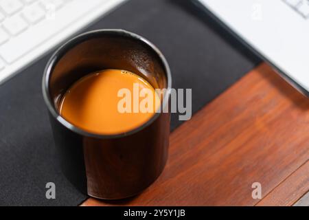 Eine warme Tasse Tee auf einem Holztisch neben einer Computertastatur. Perfekte Umgebung für eine gemütliche Arbeitsumgebung. Stockfoto