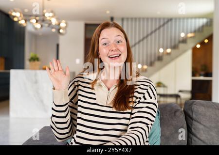 Winkend und lächelnd, Frau sitzend auf der Couch während des Treffens zu Hause, auf Videoanruf Stockfoto