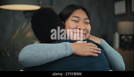 Glückliches multiethnisches Paar sitzt auf Stühlen, redet, umarmt und findet Kompromisse nach Streit über Paartherapie. Die Versöhnung liebevoller junger Familien bei der Beratung mit Psychologen oder Psychotherapeuten Stockfoto