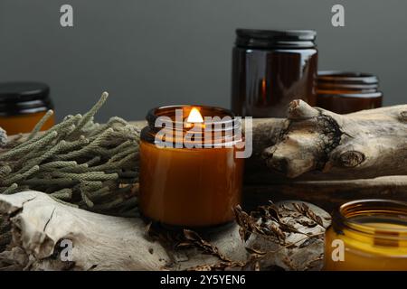 Schöne brennende Kerzen und Brunienpflanzen auf dekorativen Holzstücken vor grauem Hintergrund, Nahaufnahme Stockfoto