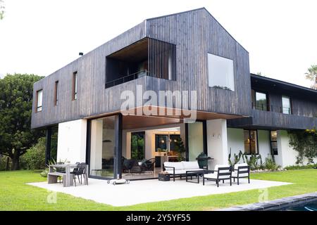 Modernes Haus mit großen Fenstern und Sitzbereich im Freien auf grünem Rasen, Kopierraum Stockfoto