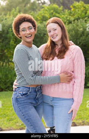 Lächelnde Freundinnen umarmen sich im Freien und genießen die gemeinsame Zeit in legeren Outfits Stockfoto