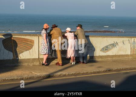 Sheringham, Norfolk, Vereinigtes Königreich - 21. SEPTEMBER 2024: In Vintage-Kleidung der 1940er Jahre gekleidete Menschen lehnen sich an die Wand und blicken auf das Meer Stockfoto