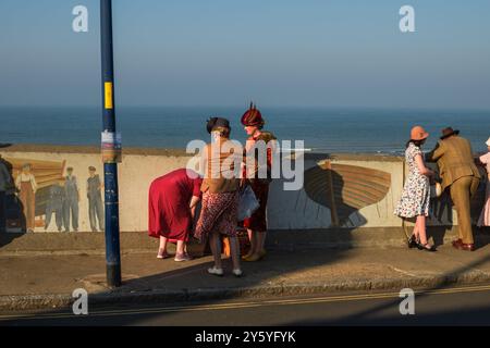 Sheringham, Norfolk, Großbritannien - 21. SEPTEMBER 2024: Frauen in Vintage-Kleidern der 1940er Jahre neben der Wand mit Blick auf das Meer Stockfoto