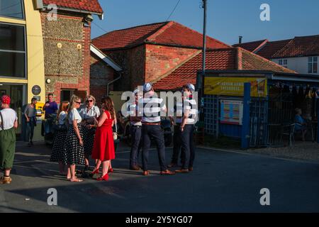 Sheringham, Norfolk, Großbritannien - 21. SEPTEMBER 2024: Gruppe der Frauen in Vintage-Kleidern der 1940er Jahre und Gruppe von Matrosen im Gespräch Stockfoto